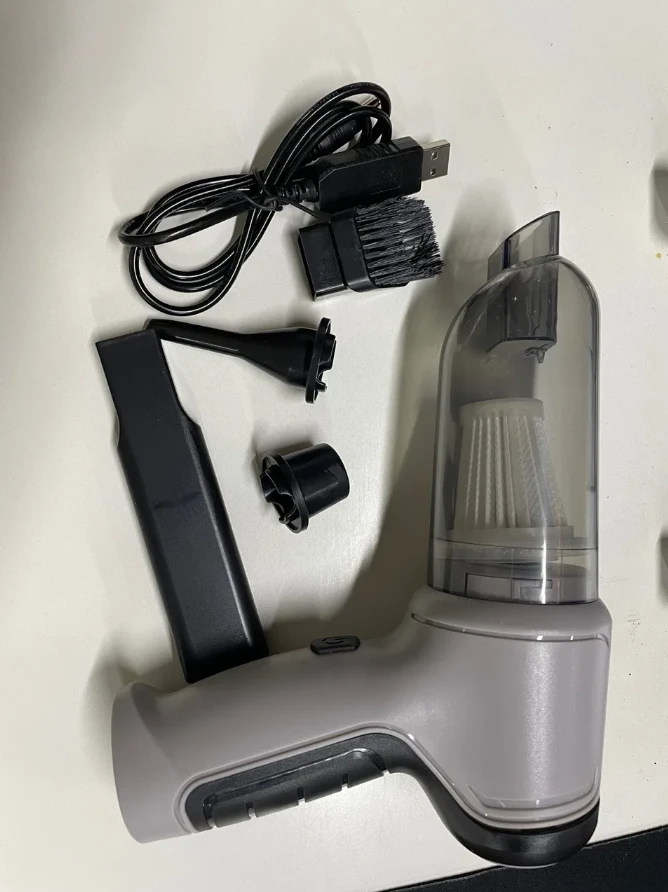 Foto real do aspirador portátil cinza com reservatório transparente, bicos, escova e cabo USB